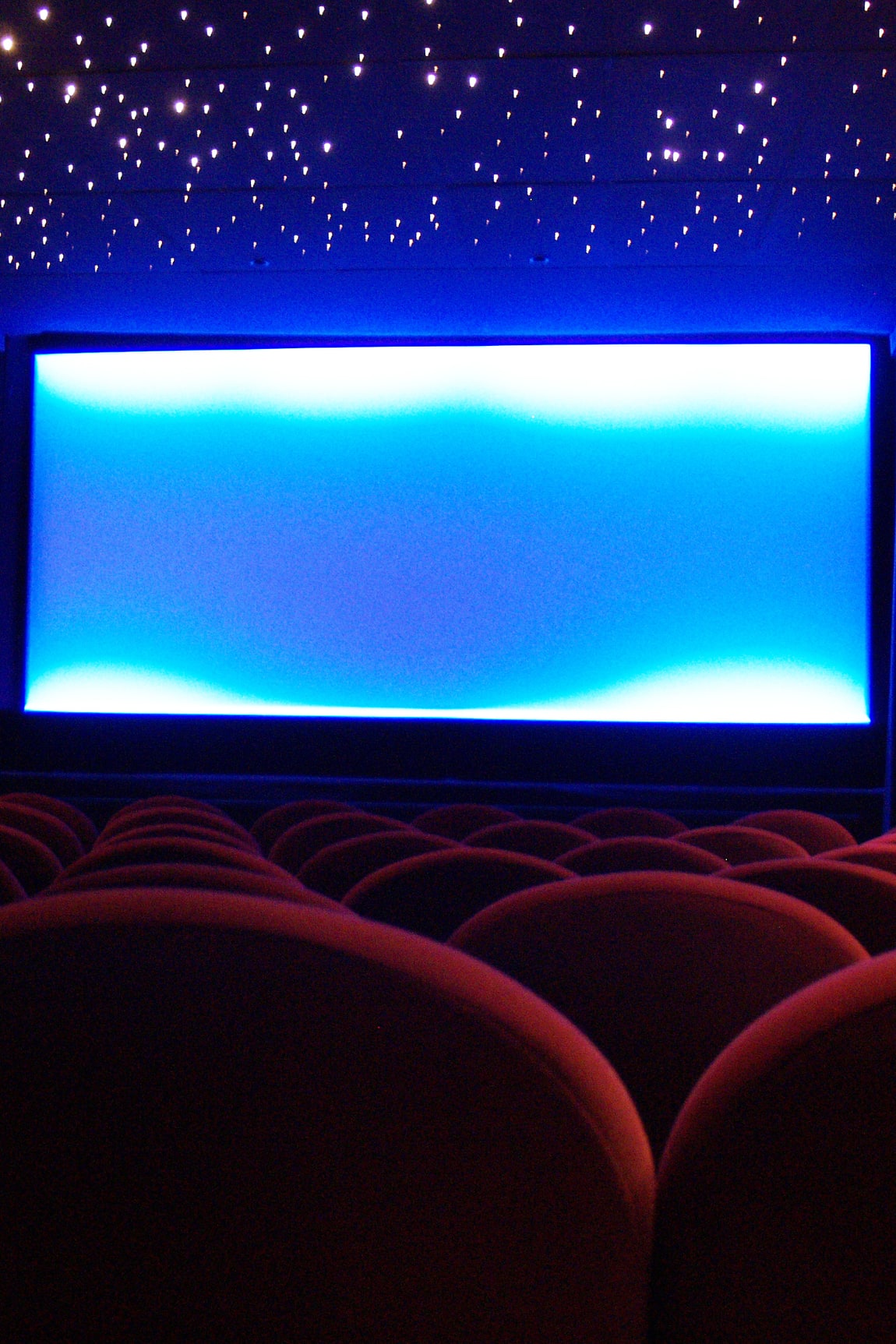 The red seats and blue-lit screen of a Paris art-house cinema before the film, under a ceiling of small lights.